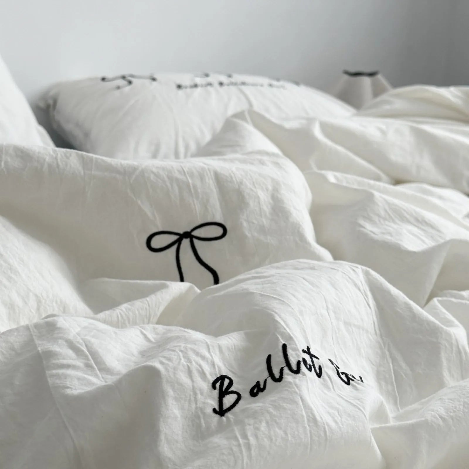 A soft-focus shot of the crinkled white washed cotton bedding, showing the delicate black bow embroidery. - RoomDen