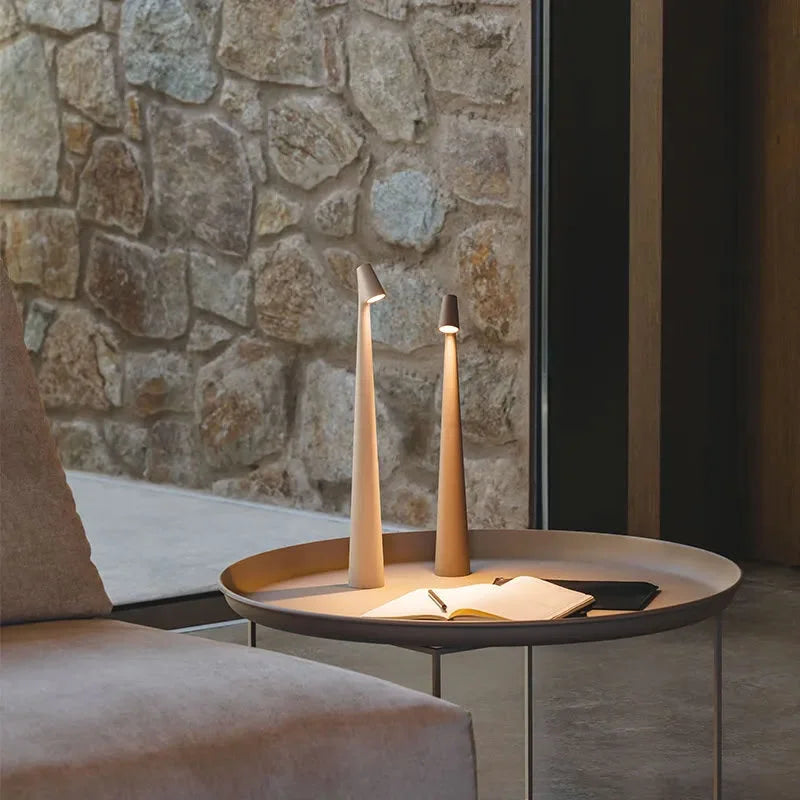 Two cordless accent lamps in a warm beige finish on a metal side table against a rustic stone wall, creating a cozy ambiance - RoomDen.