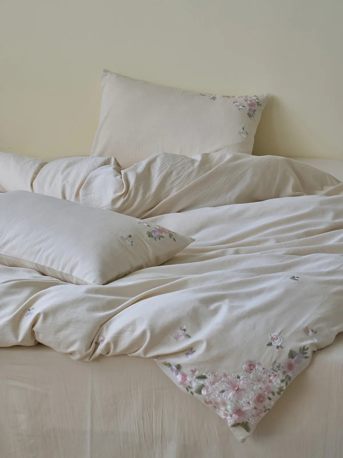 Close-up of the corner of the Intricate Wildflower Embroidered Linen Bedding Set in vintage cream, showing detailed pink floral embroidery. - RoomDen