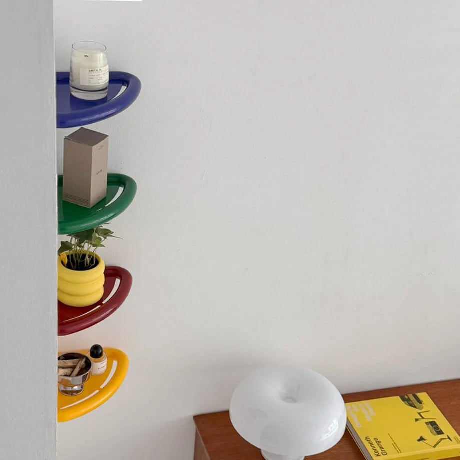 A stack of colorful blue, green, red, and yellow corner shelves seen from the side, with a white lamp and books nearby. - RoomDen