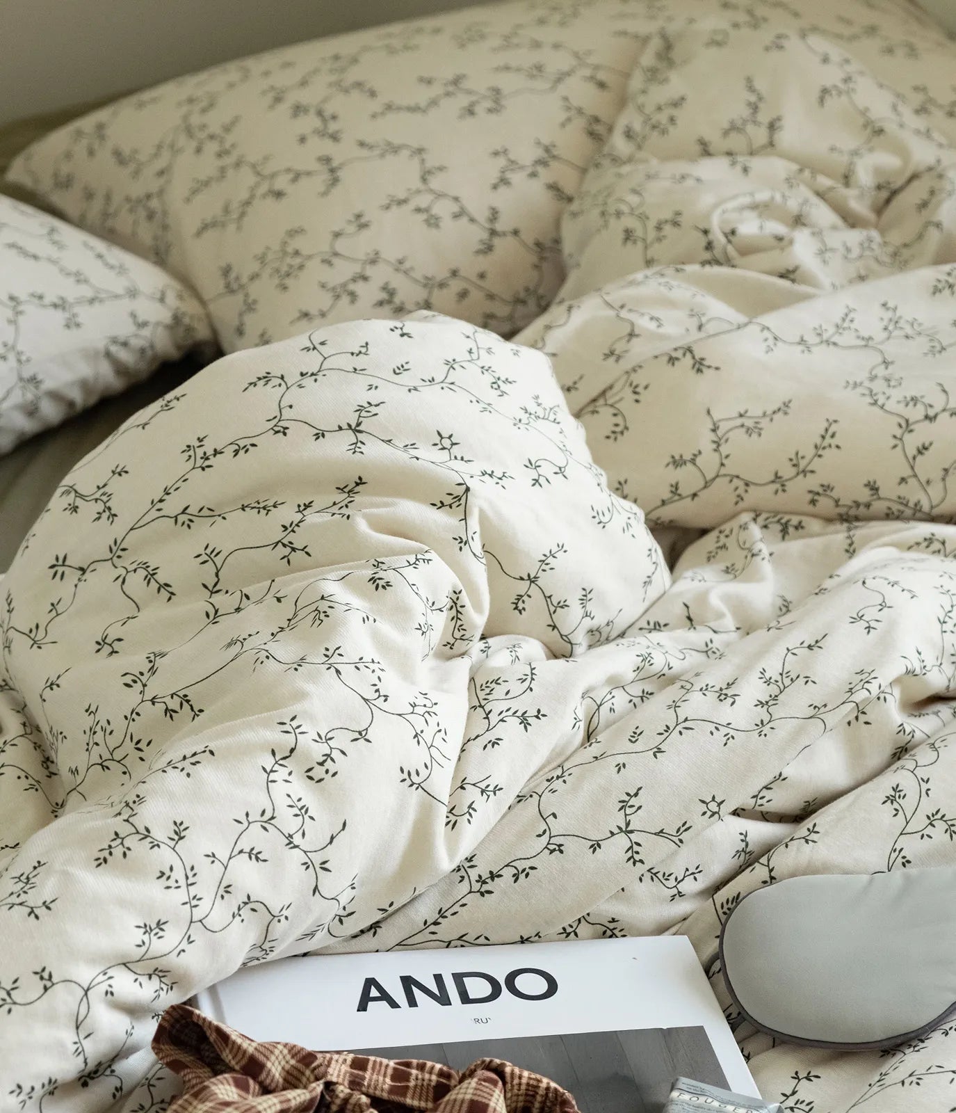 Close-up lifestyle shot of the Soft Dainty Vine Washed Cotton Bedding Set, showing its texture with a book and eye mask. - RoomDen