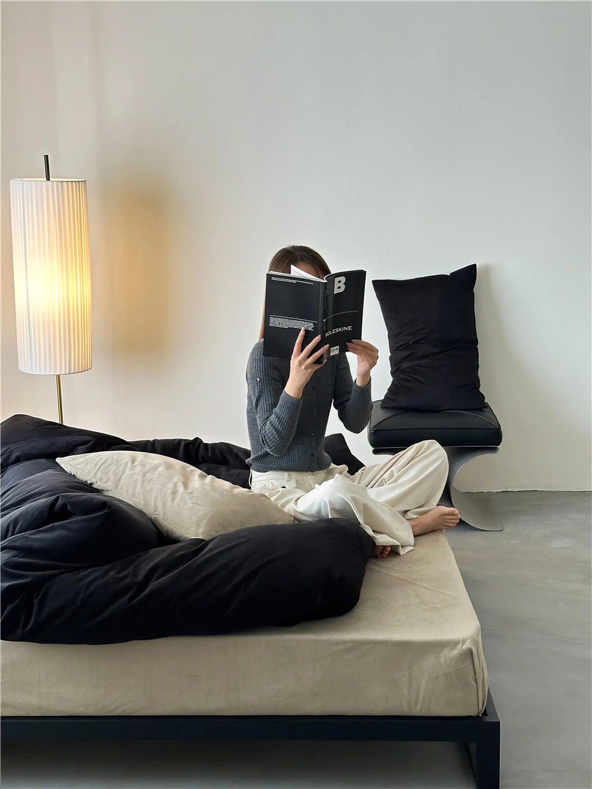 Woman reading a book in bed, surrounded by the soft Obsidian Black & Cream velvet bedding set. - RoomDen