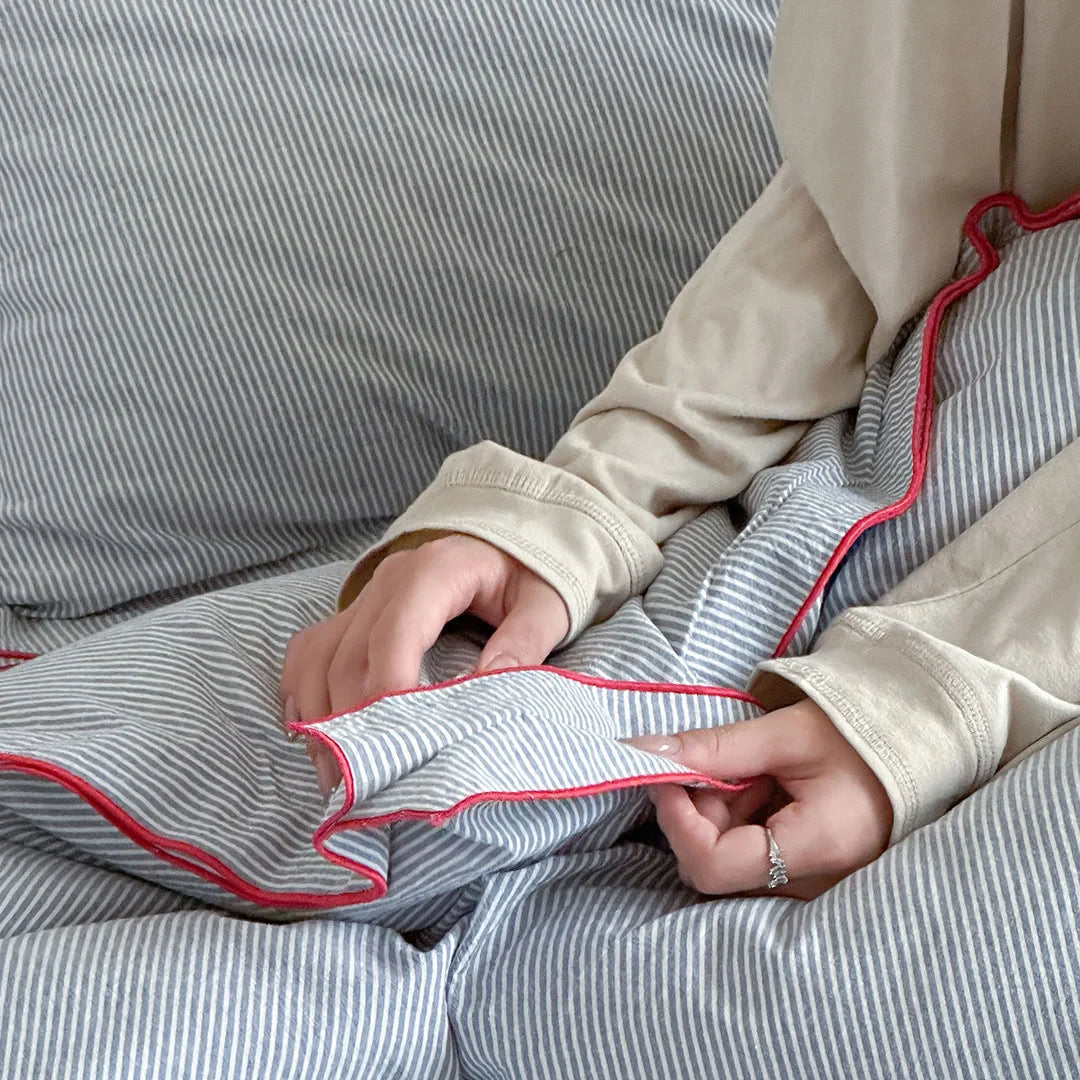 Close-up detail of hands touching the red ruffle edge of the pinstripe washed cotton duvet cover.