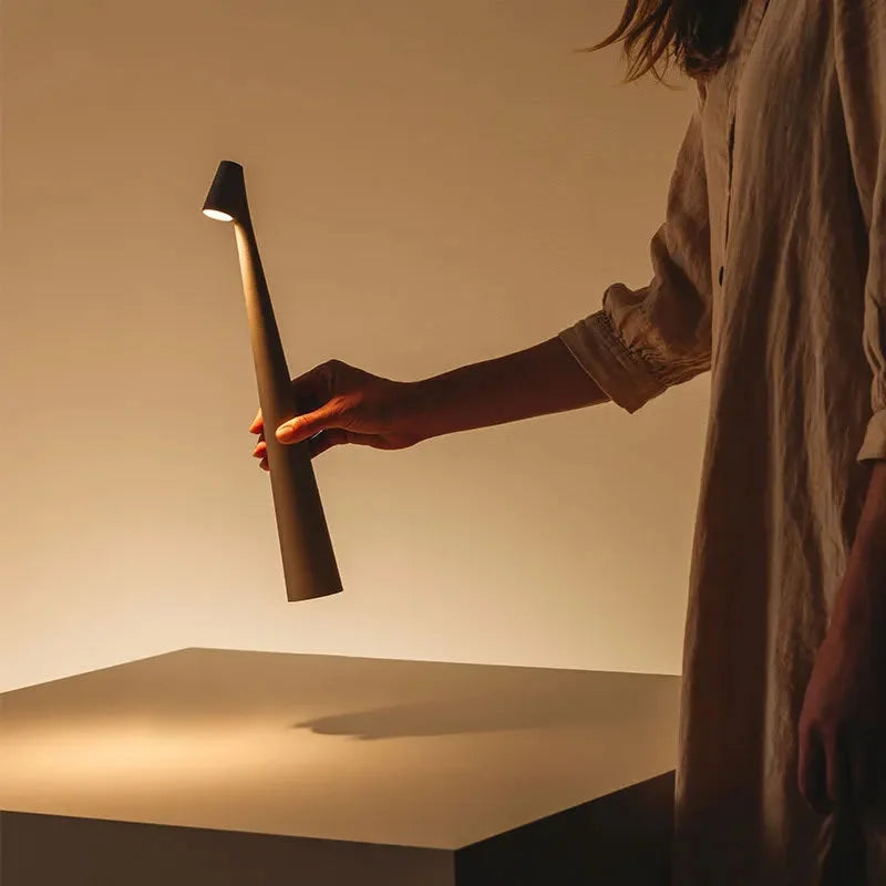 A hand holding the sleek, portable taupe grey cordless lamp, demonstrating its minimalist design and mobility - RoomDen.