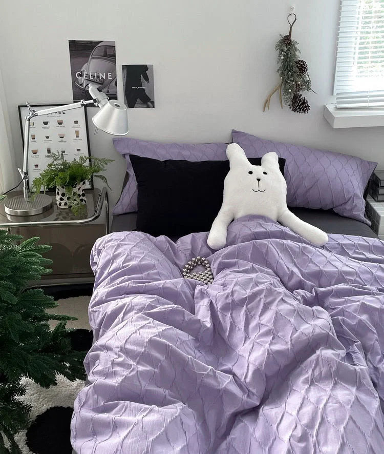 A lavender ruched pintuck bedding set styled in a cozy bedroom with a white bunny plushie. - RoomDen