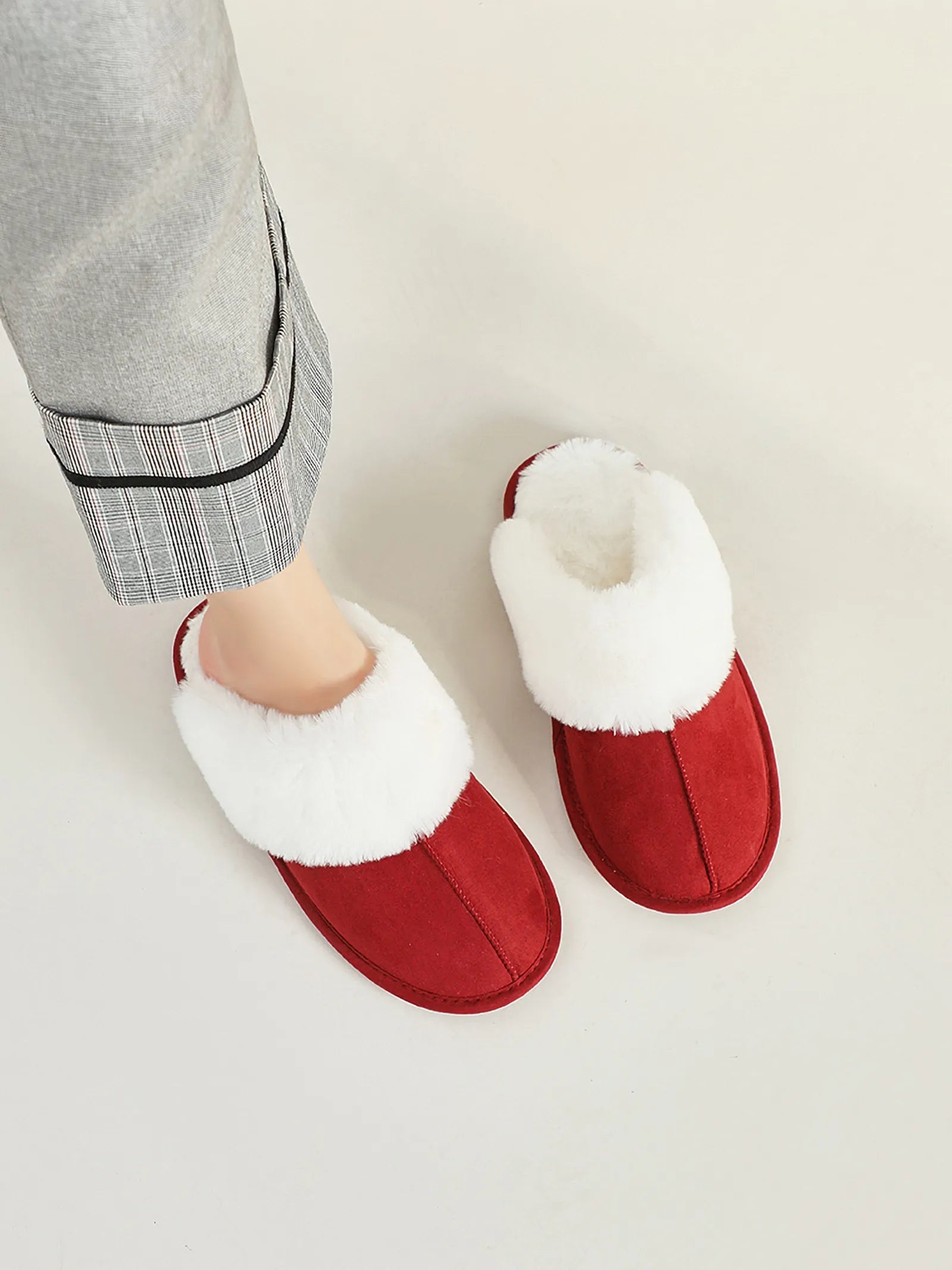 Close-up of Red Faux Suede House Slippers on feet with grey plaid trousers.