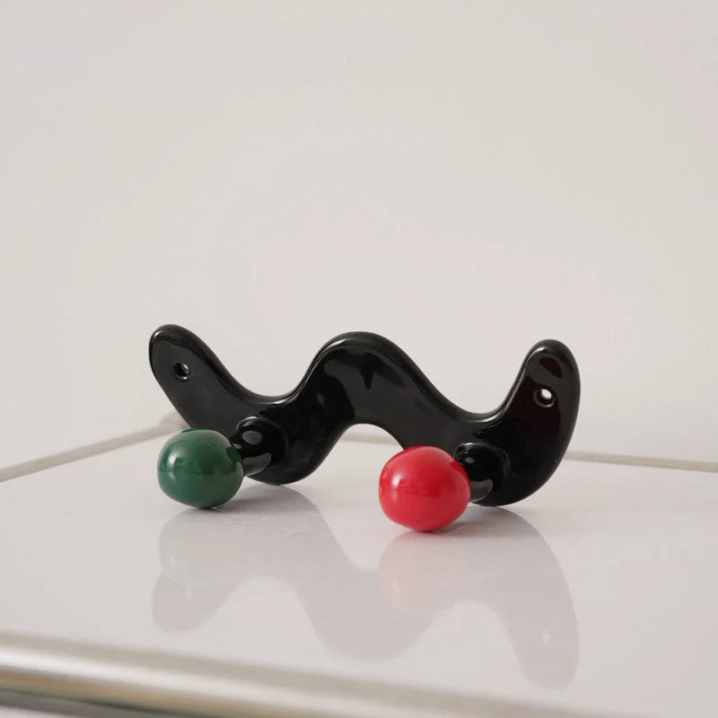 Glossy black wavy ceramic hook with one green and one red ball.