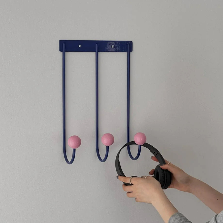 Detailed shot of hands placing headphones onto the Blue & Pink U-shaped metal wall hooks. - RoomDen
