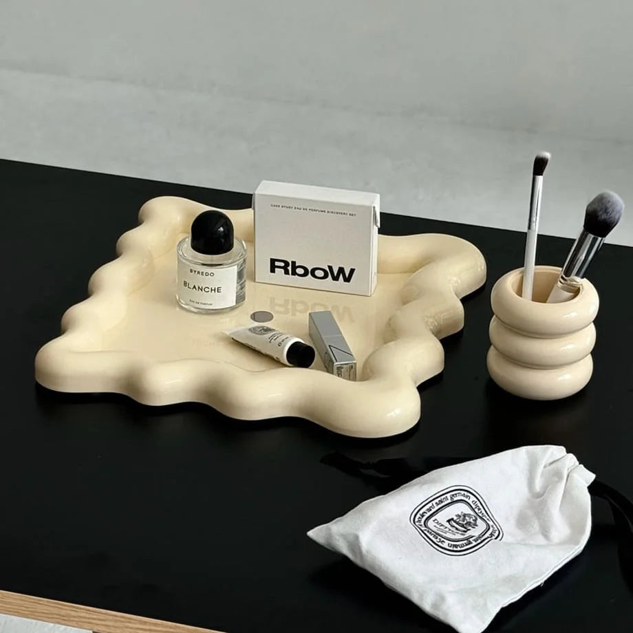 Cream wavy jewelry tray holding perfume and makeup on a black desk - RoomDen