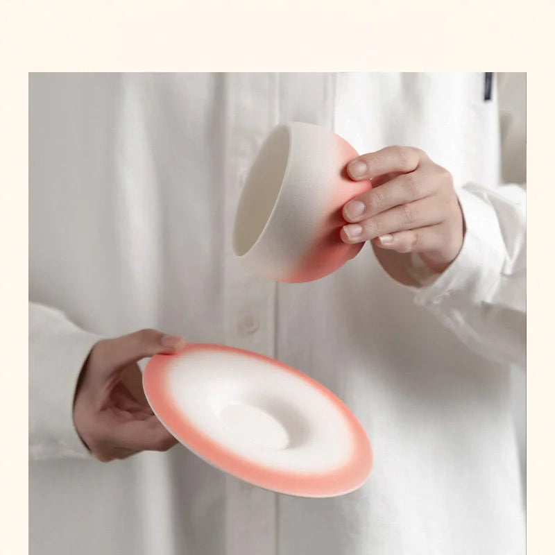 Hands holding the Blush Pink Matte Ombre Ceramic Cup and Saucer. - RoomDen