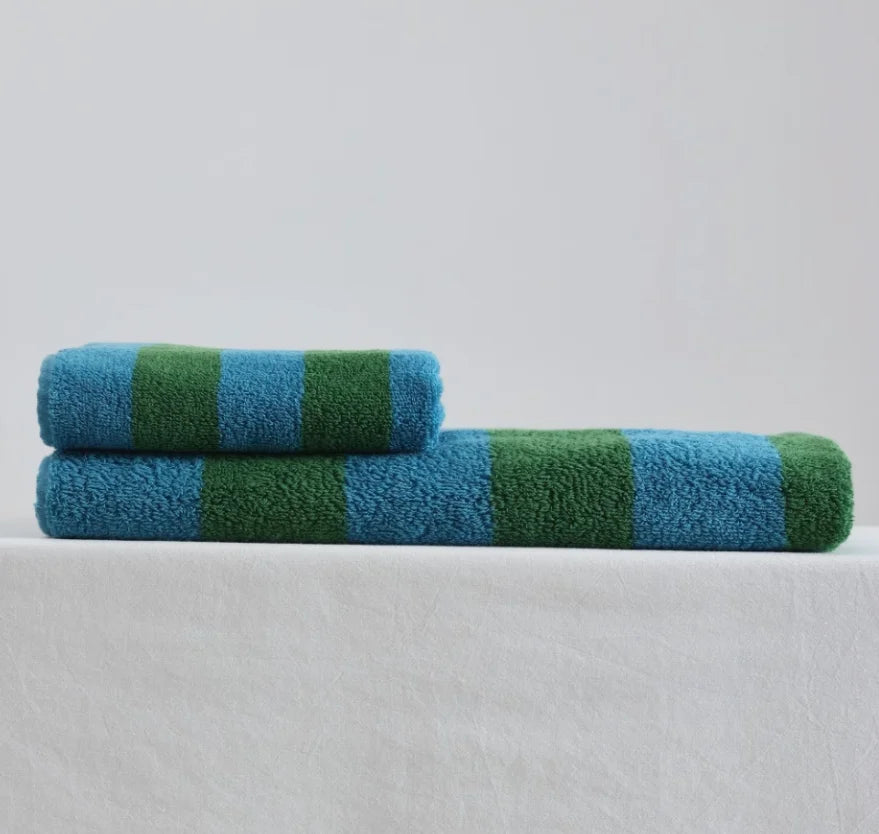 A plush blue and green striped cotton bath towel and face towel neatly folded on a white surface. - RoomDen