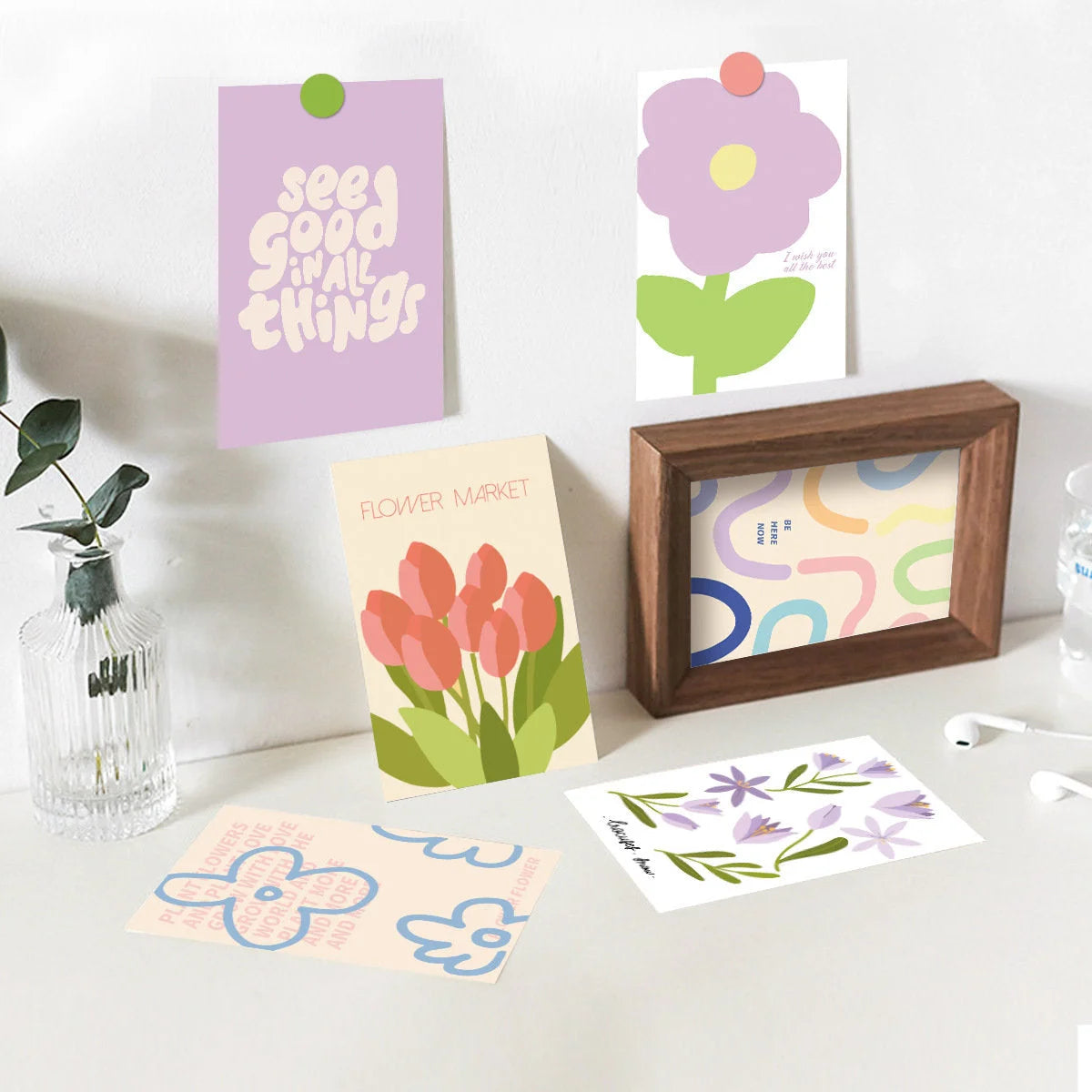 Several cards from the Vibrant Danish Pastel Wall Collage Kit styled on a desktop with a picture frame and a small vase. - RoomDen
