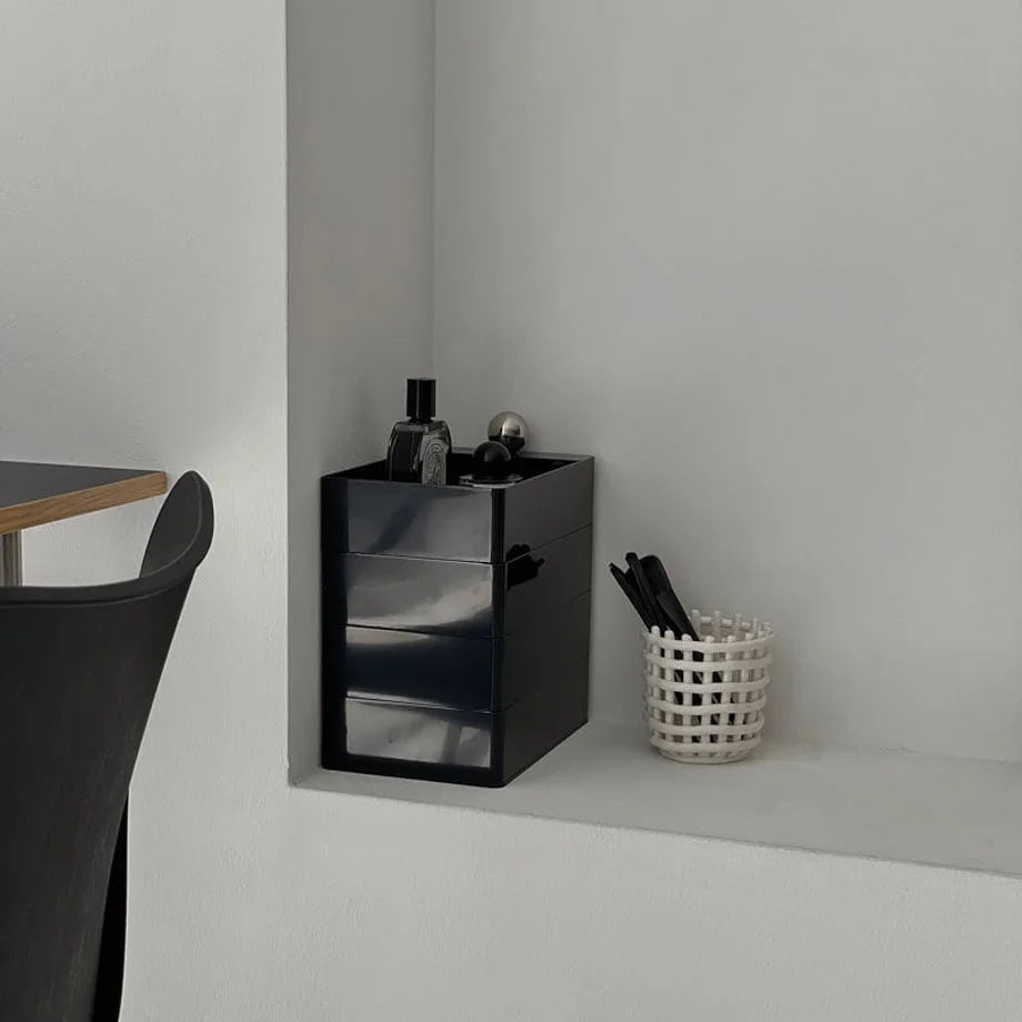 Black rotating makeup organizer in a closed position, styled in a minimalist white nook.