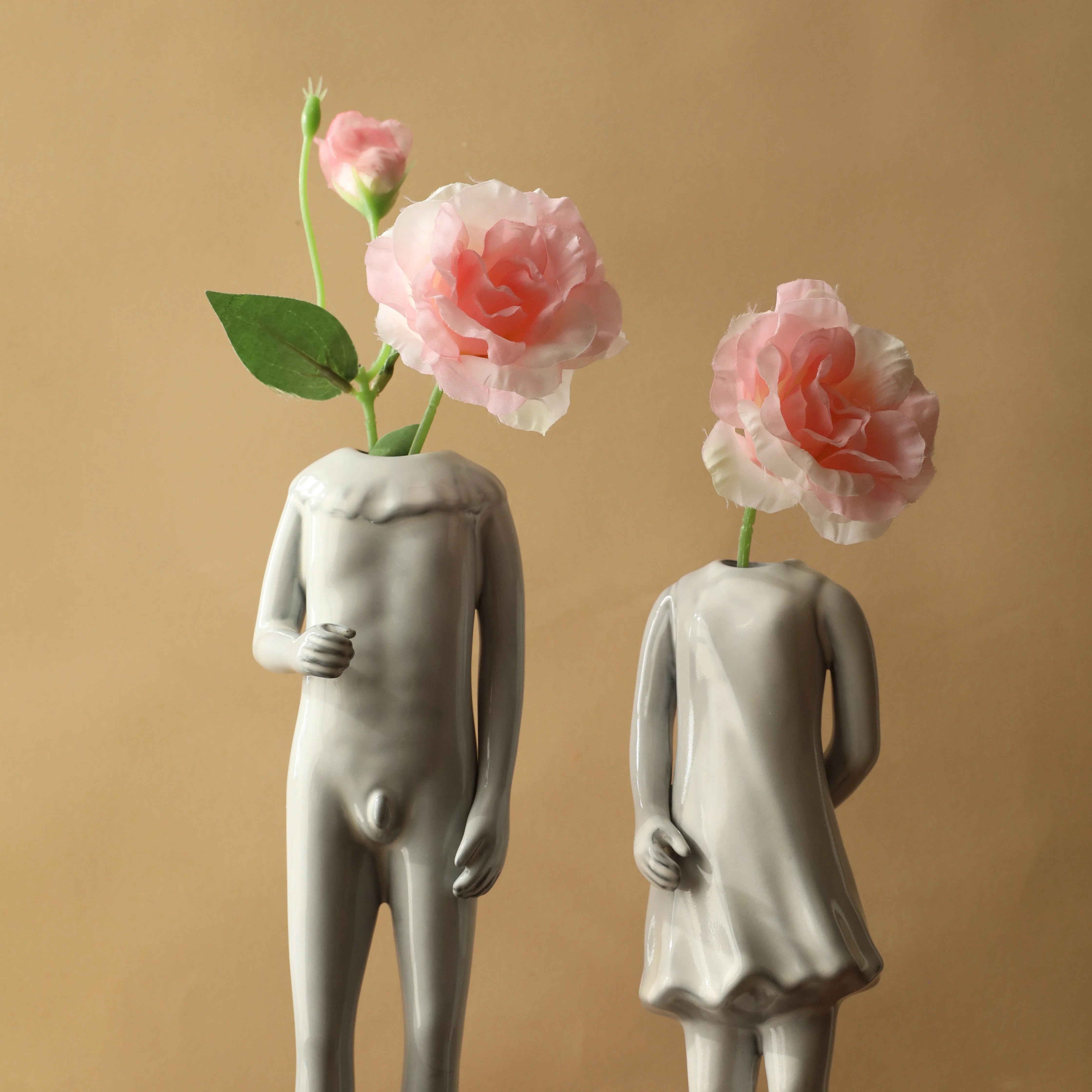 The male and female figure ceramic vases styled together, each holding a single pink rose. - RoomDen