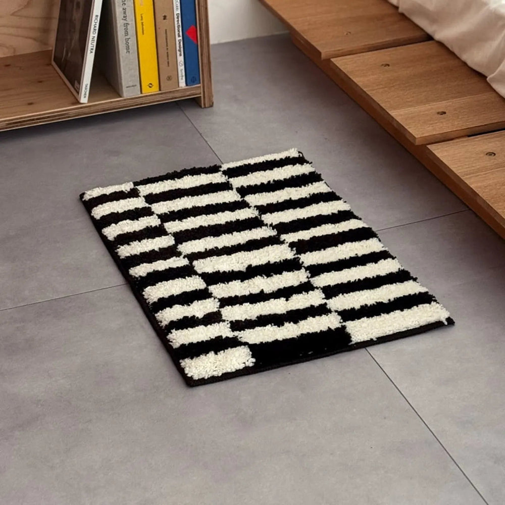 Plush shaggy accent rug featuring a bold black and white offset stripe pattern on a grey floor - RoomDen