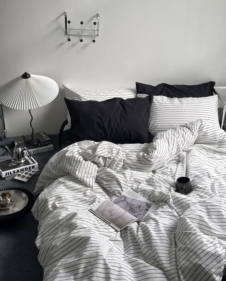 Full view of a bed with a textured pinstripe washed cotton bedding set, styled with black pillows and a modern pleated lamp. - RoomDen