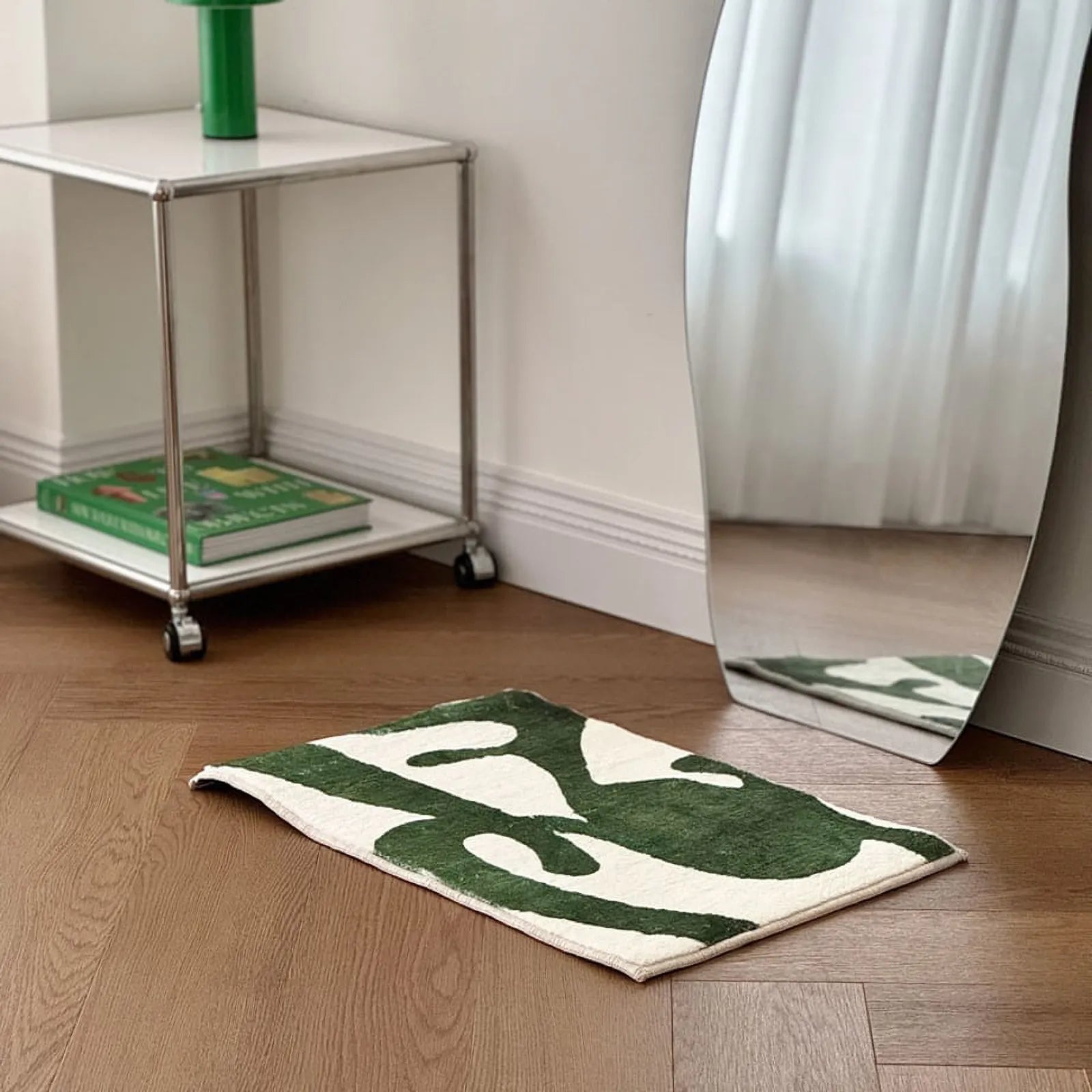 Green & White abstract accent rug placed near a chrome side table and wavy mirror