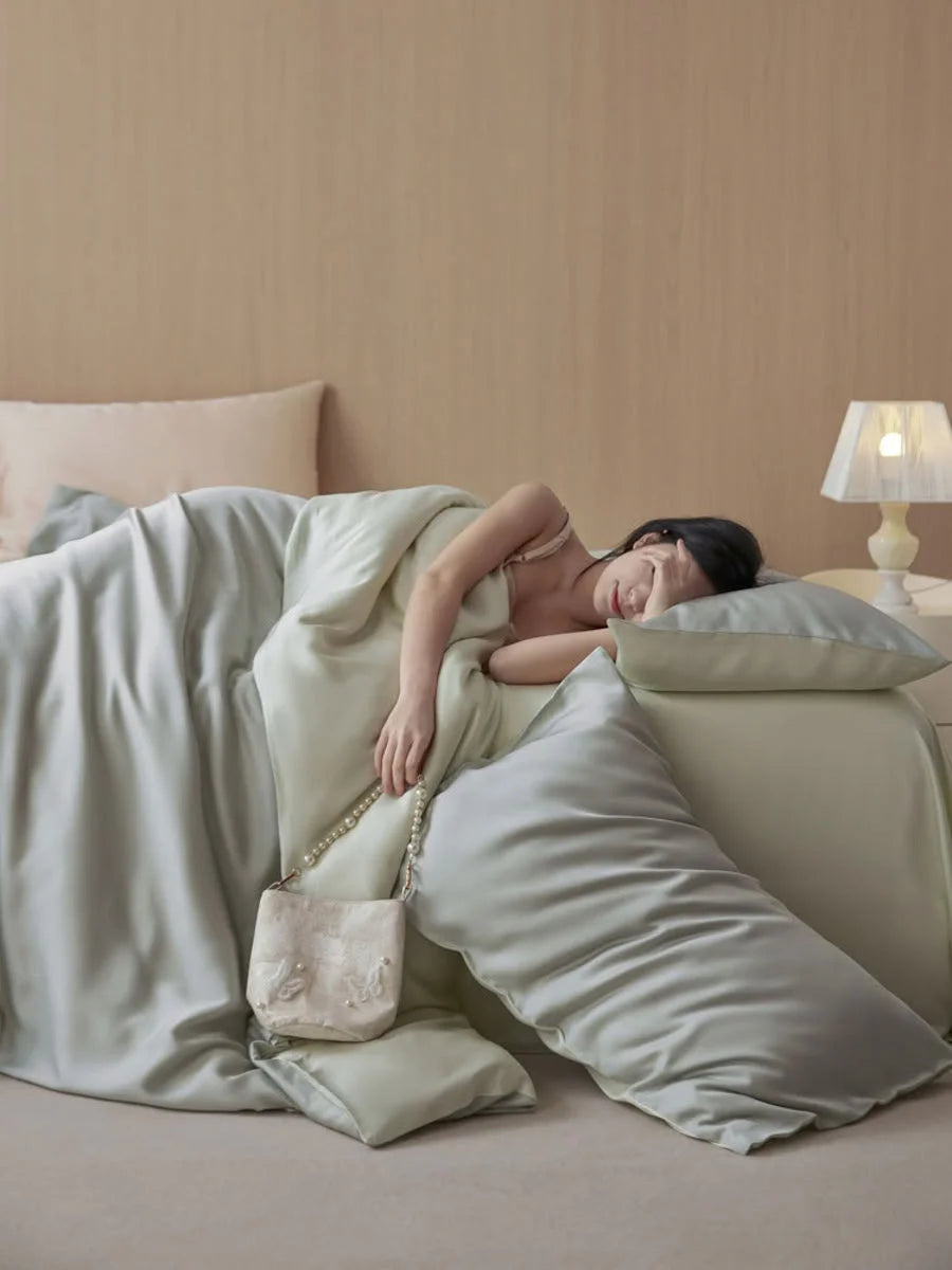 A person resting in bed with the Sage Mist Tencel bedding, showing its comfortable and soft drape. - RoomDen