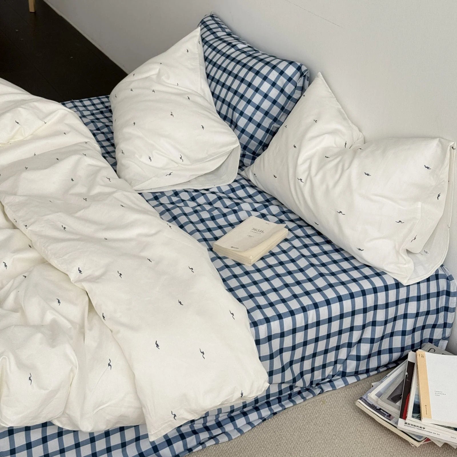 Angled view of the Gingham & Seagull bedding set with a book resting on the blue checkered sheet - RoomDen