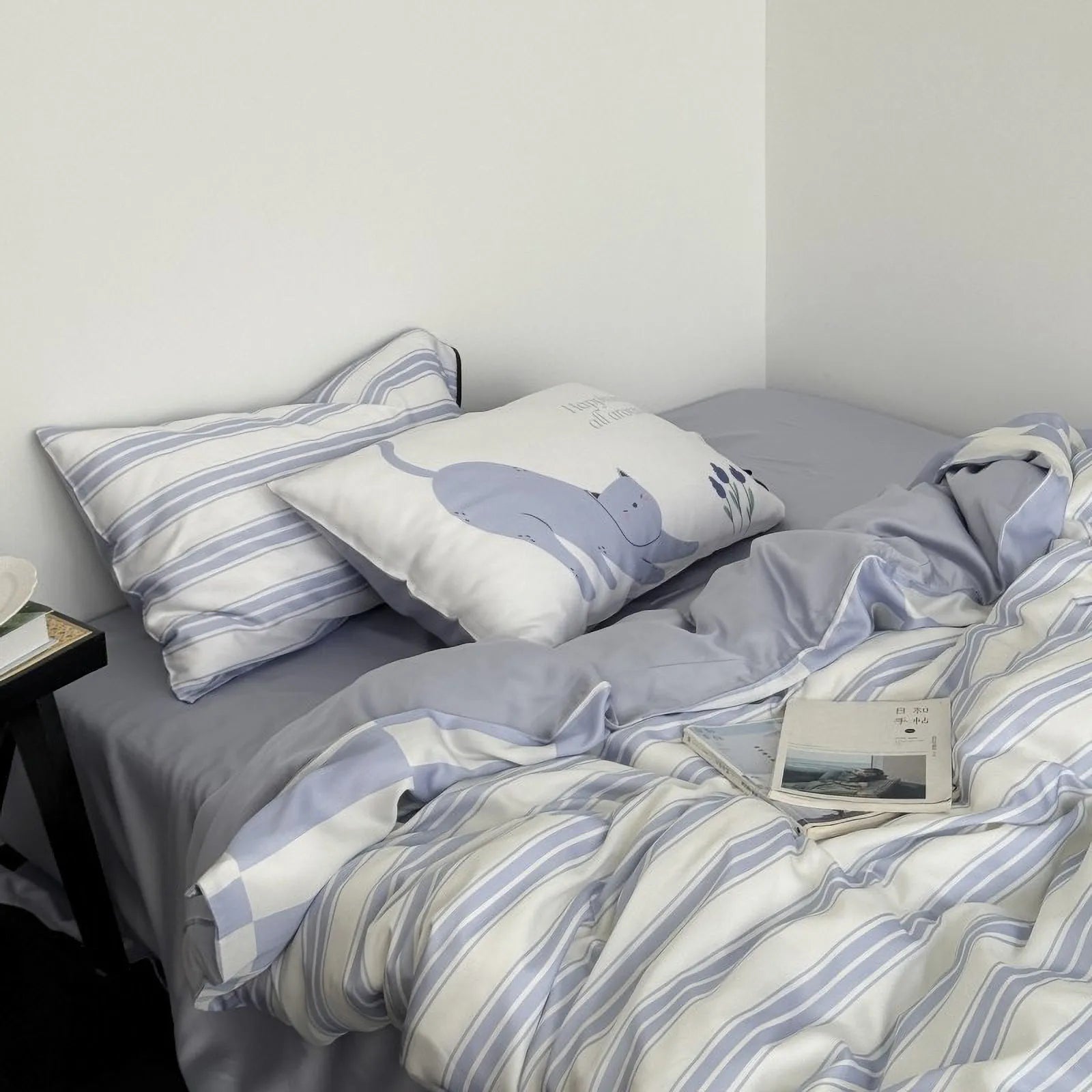 Close-up of the Cat & Stripe Washed Cotton Bedding Set showing the striped pillowcase and cute cat pillow on a periwinkle blue sheet. - RoomDen