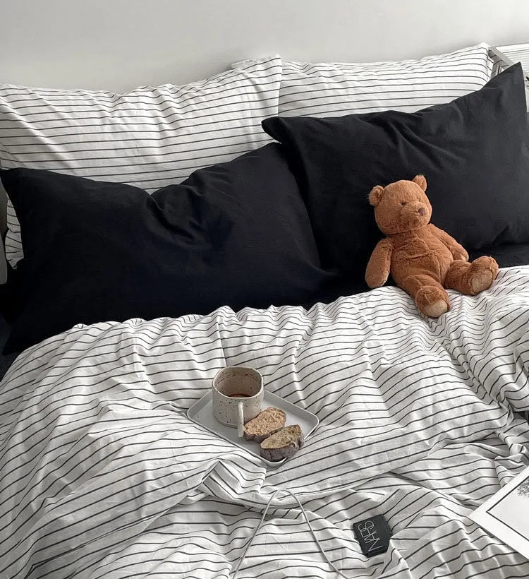A cozy bed scene with the pinstripe bedding set, black pillows, and a teddy bear, with a breakfast tray on the duvet. - RoomDen