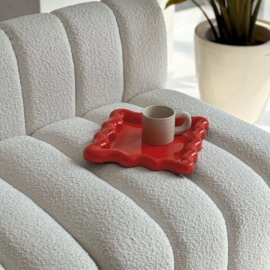 Lifestyle image of the Cherry Red wavy tray on a textured sofa in a sunlit room - RoomDen
