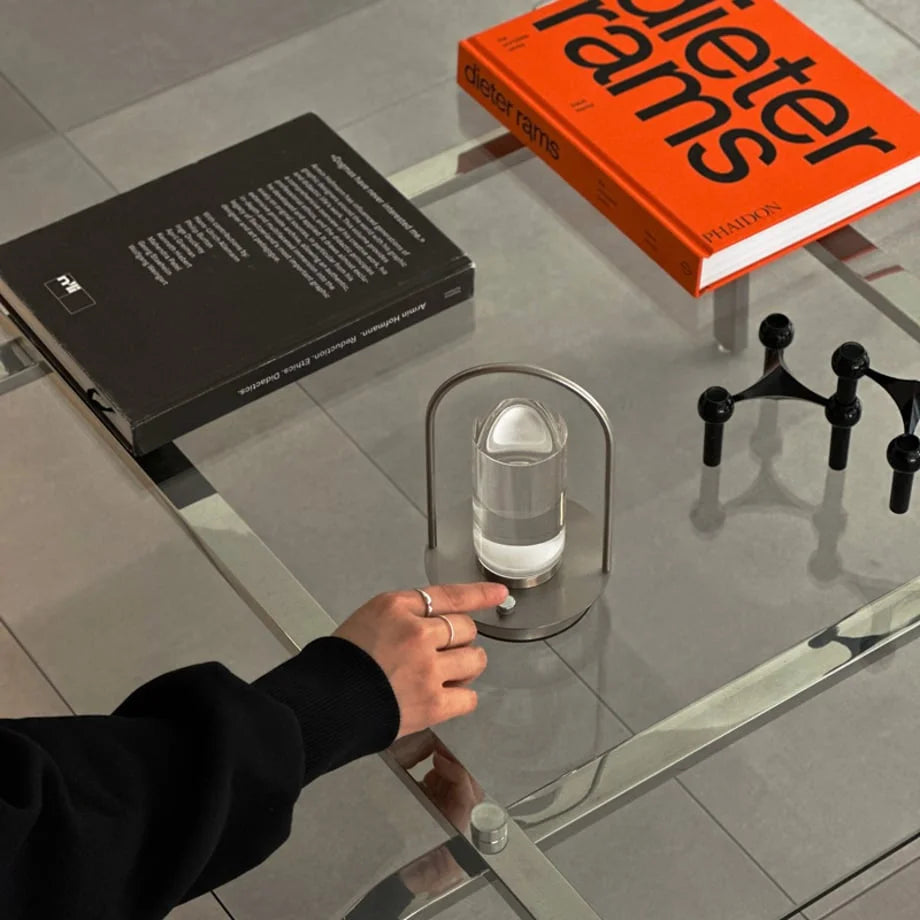 A hand touching the power button of the Minimalist Arch Metal Table Lamp. - RoomDen