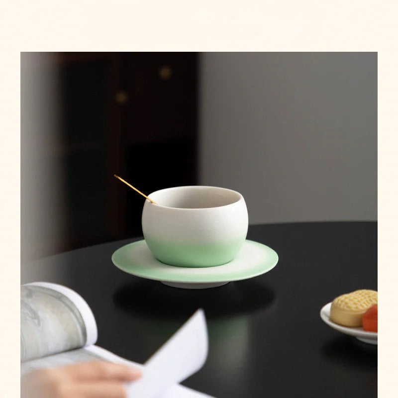 The Mint Green Ombre Ceramic Cup and Saucer on a dark table, ready for a coffee break. - RoomDen