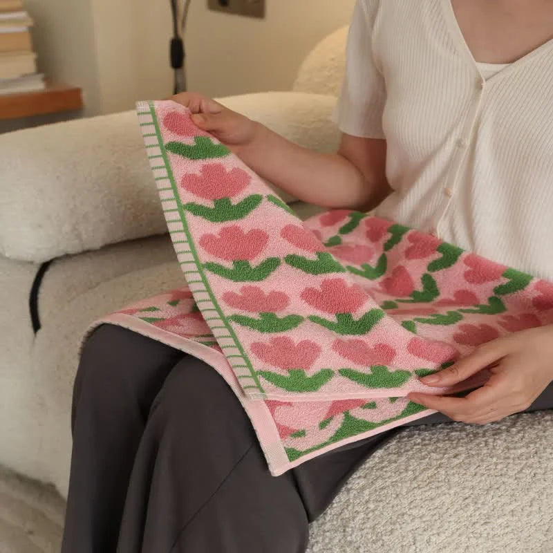 A woman sitting on a boucle sofa, feeling the soft texture of the pink Tulip Floral Cotton Face Towel - RoomDen