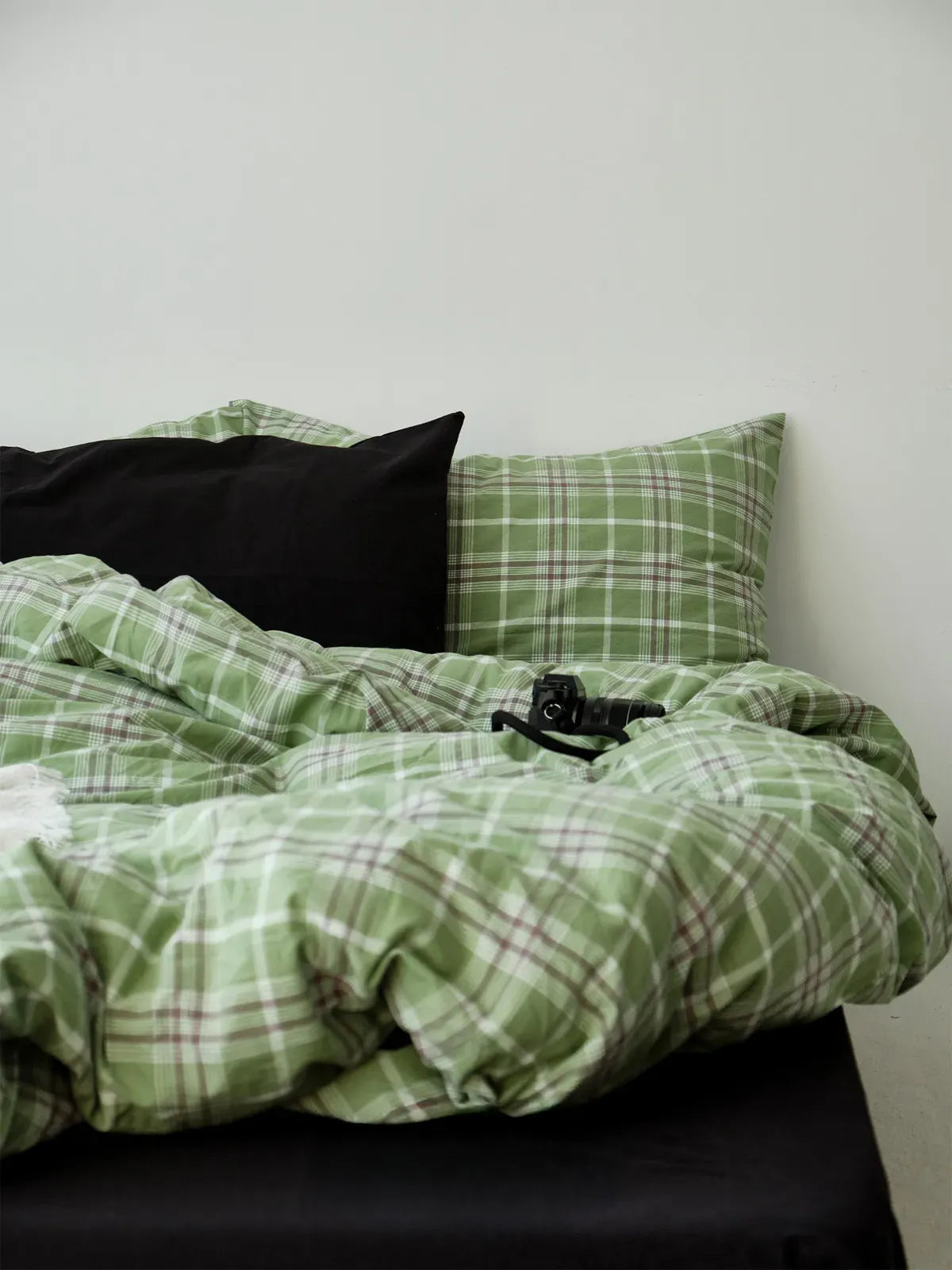The green plaid duvet cover and pillowcases styled with a contrasting black sheet and pillow, showing the texture of the washed cotton. - RoomDen