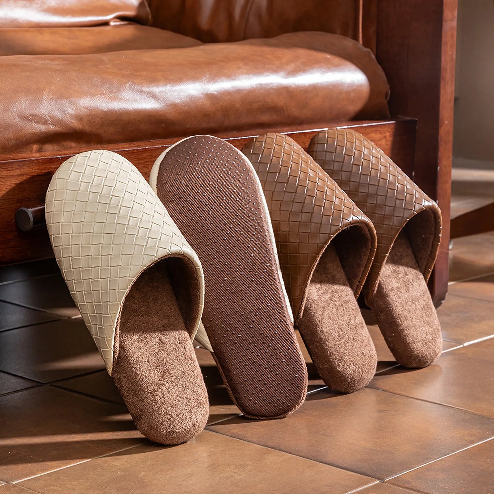 Soles of beige and brown slippers showing non-slip texture against a leather sofa