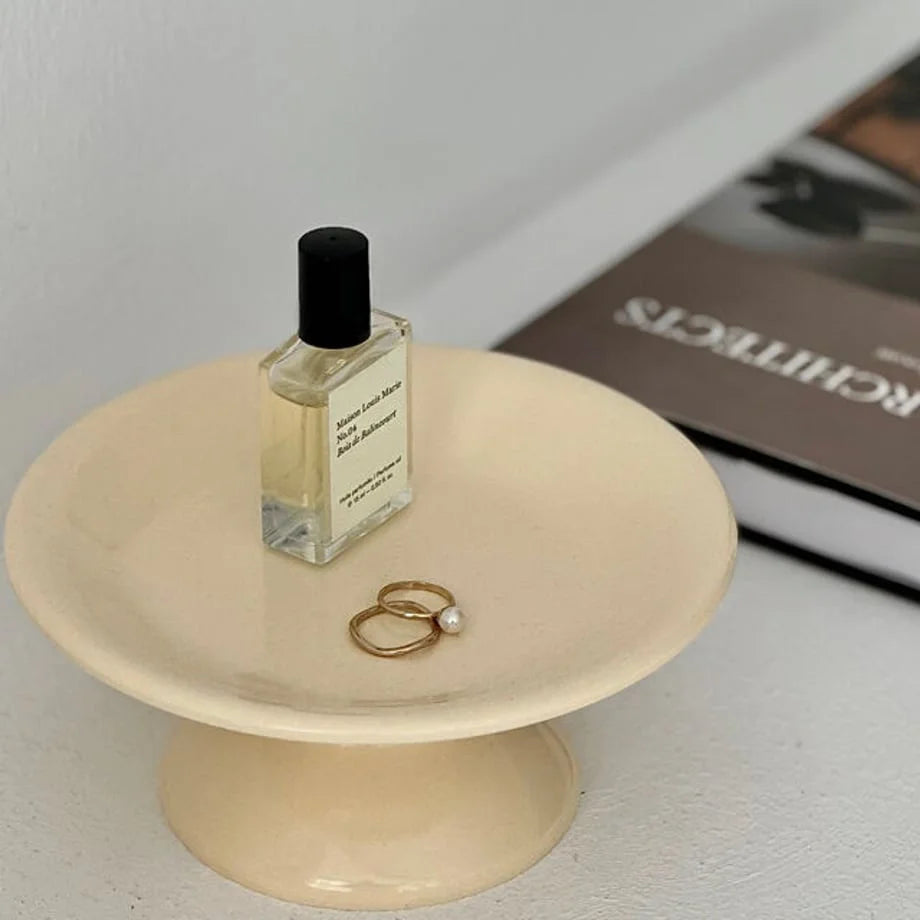 Detailed close-up on the two rings sitting in the creamy beige pedestal dish. - RoomDen