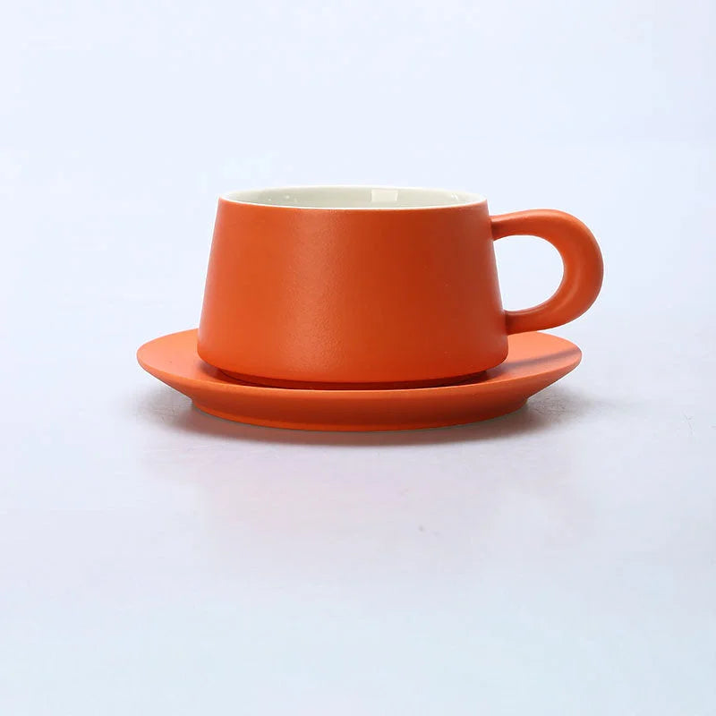 Front view of the Marigold Orange matte ceramic coffee cup and saucer set against a white background. - RoomDen