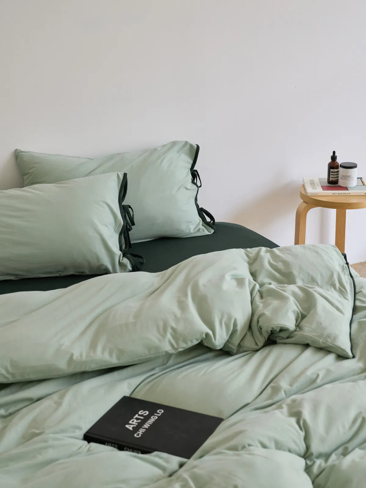 Lifestyle view of the Sage Green & Black washed cotton bedding set in a bright, minimalist bedroom. - RoomDen