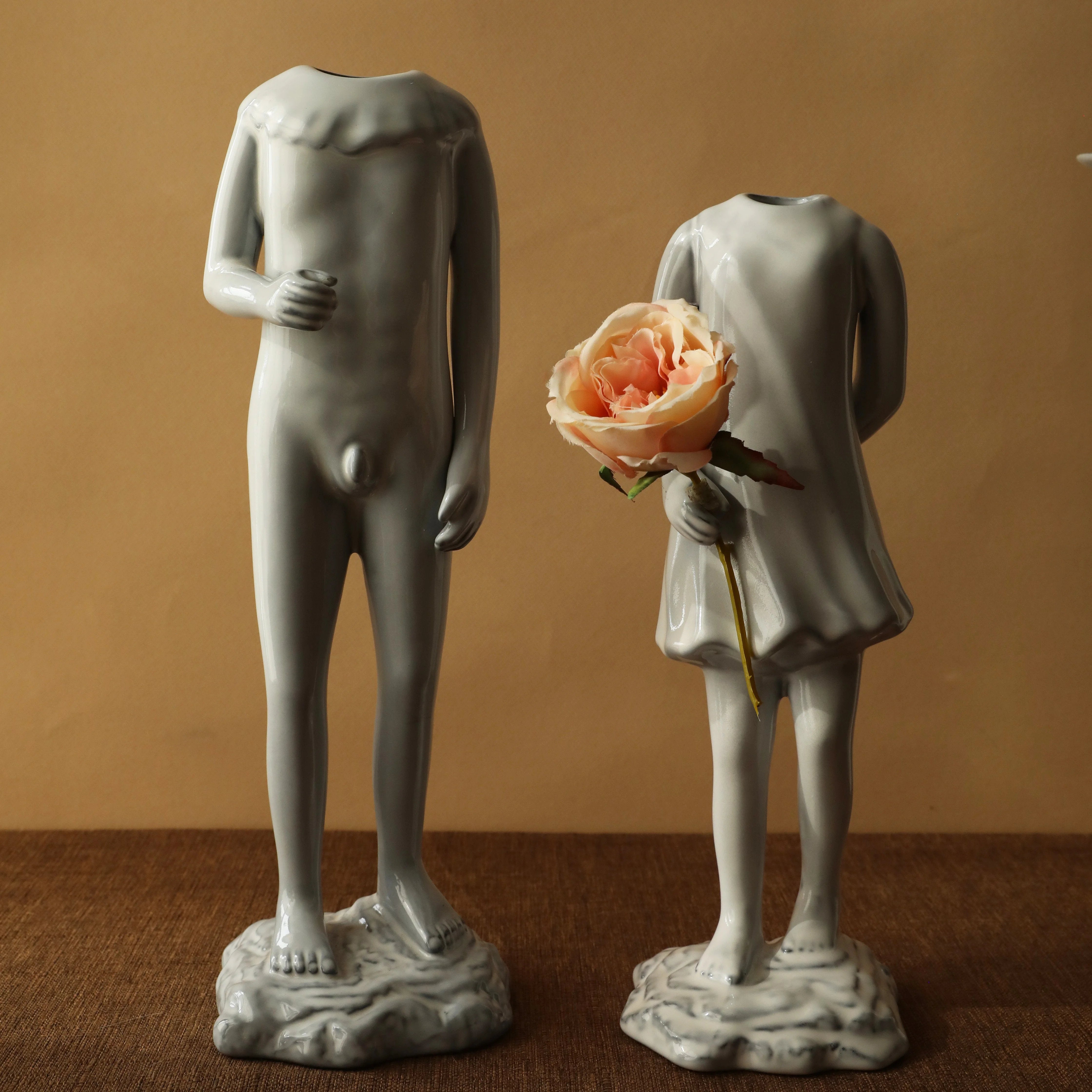 The male and female ceramic figure vases standing side-by-side, one holding a peach rose. - RoomDen