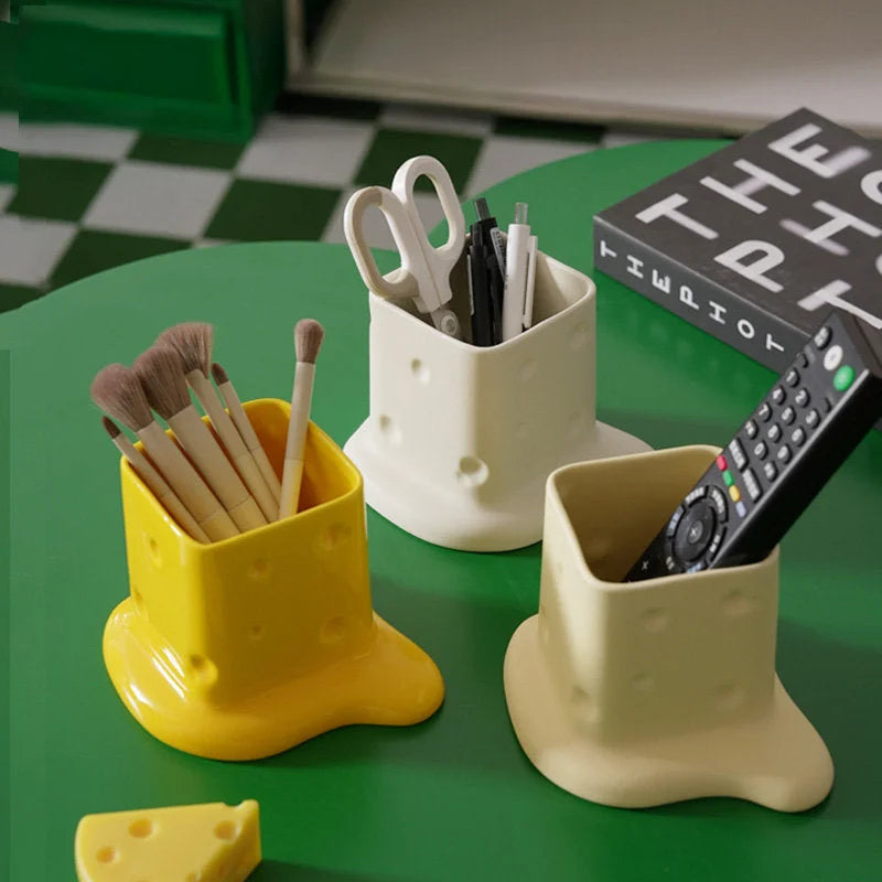 Three melting cheese ceramic organizers in yellow, cream, and beige, holding pens, brushes, and a remote on a green table. - RoomDen