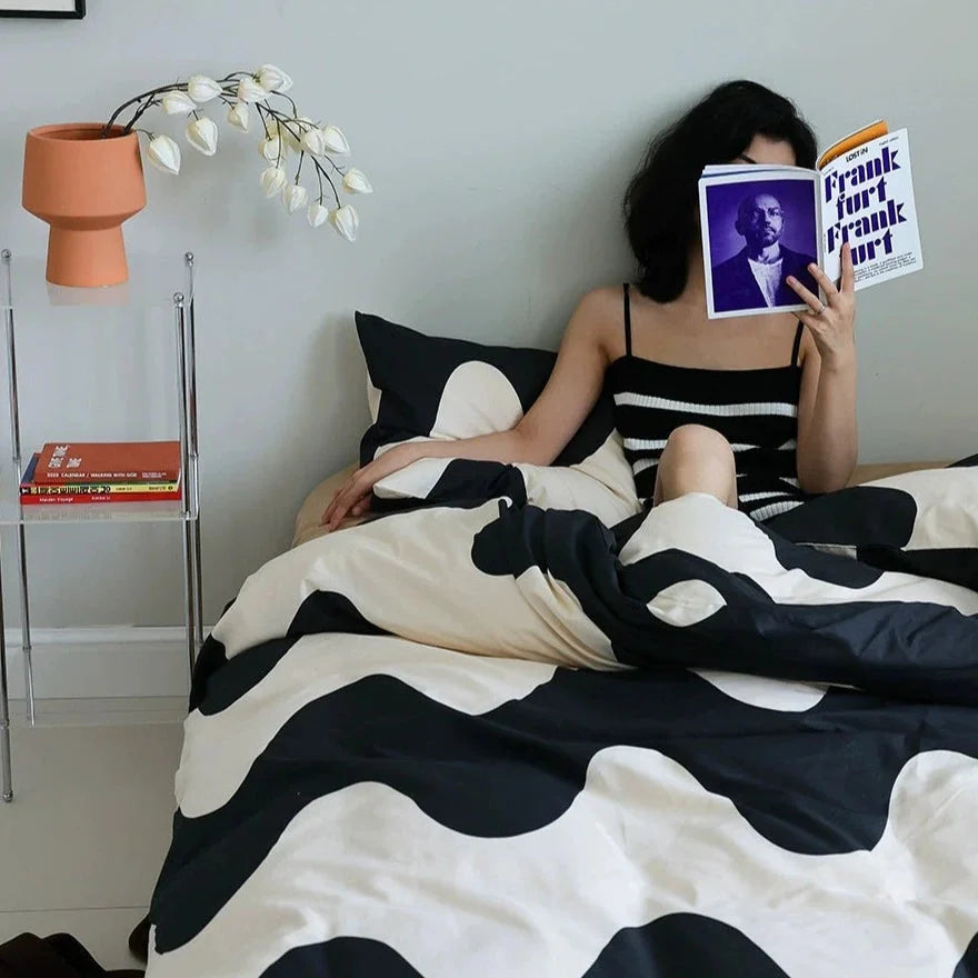 Model reading in bed with the Smooth Wavy Abstract Cotton Bedding Set featuring a bold black and beige pattern - RoomDen