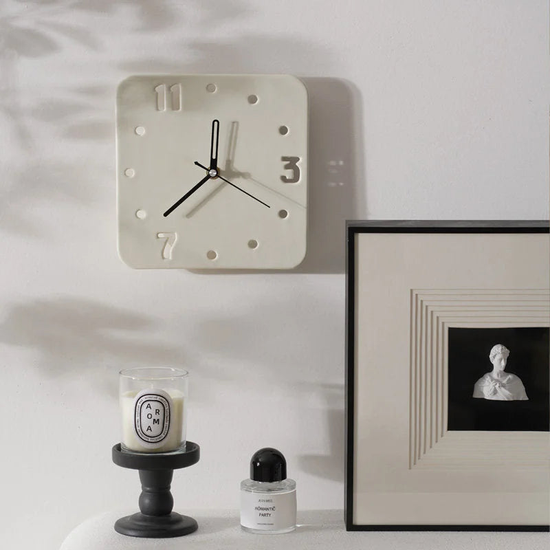 Cream ceramic cutout clock mounted on a white wall above a Diptyque candle and framed art - RoomDen.