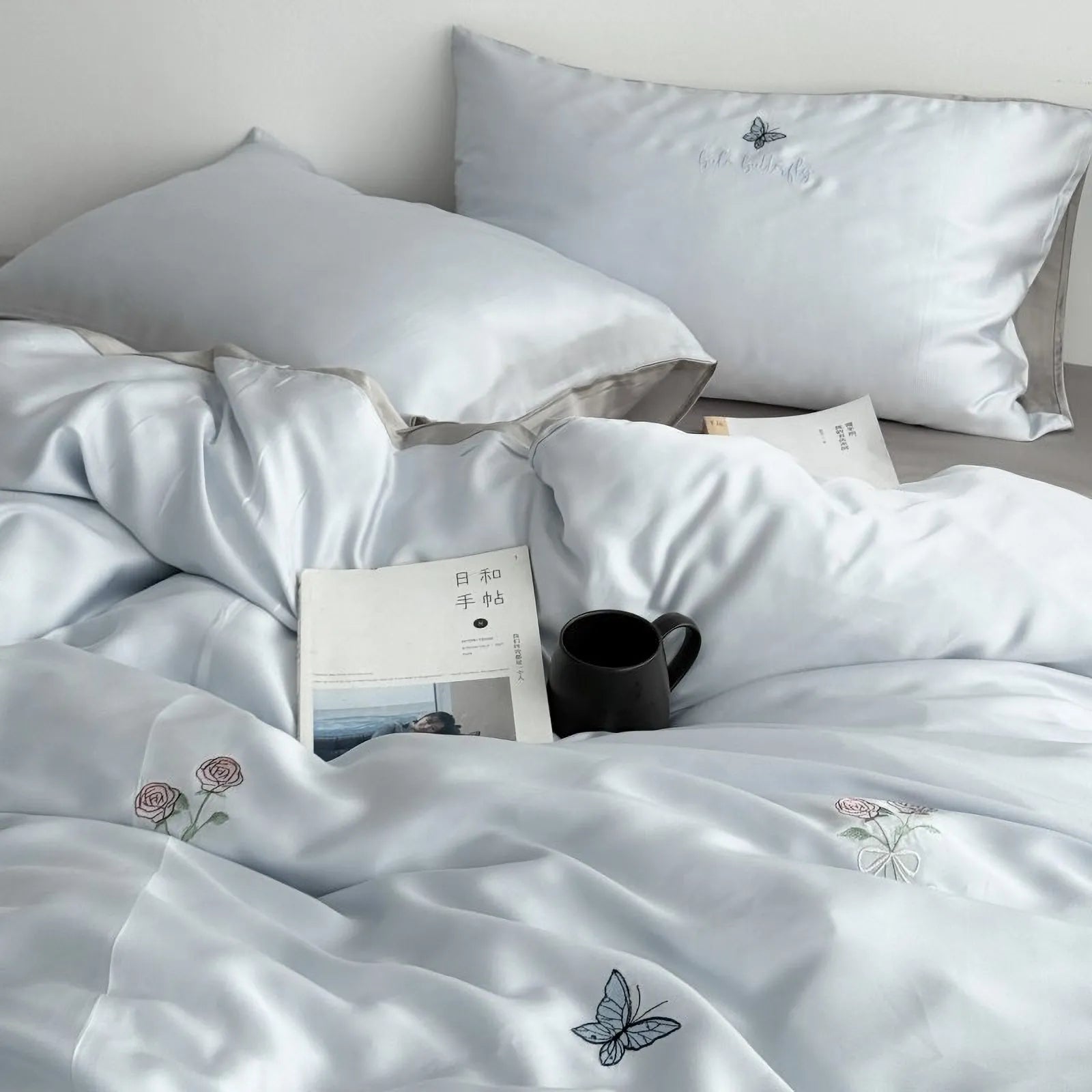 Angled view of the Cloud Blue Tencel bedding set, showing the silky sheen and embroidered details on the duvet cover and pillowcase.
