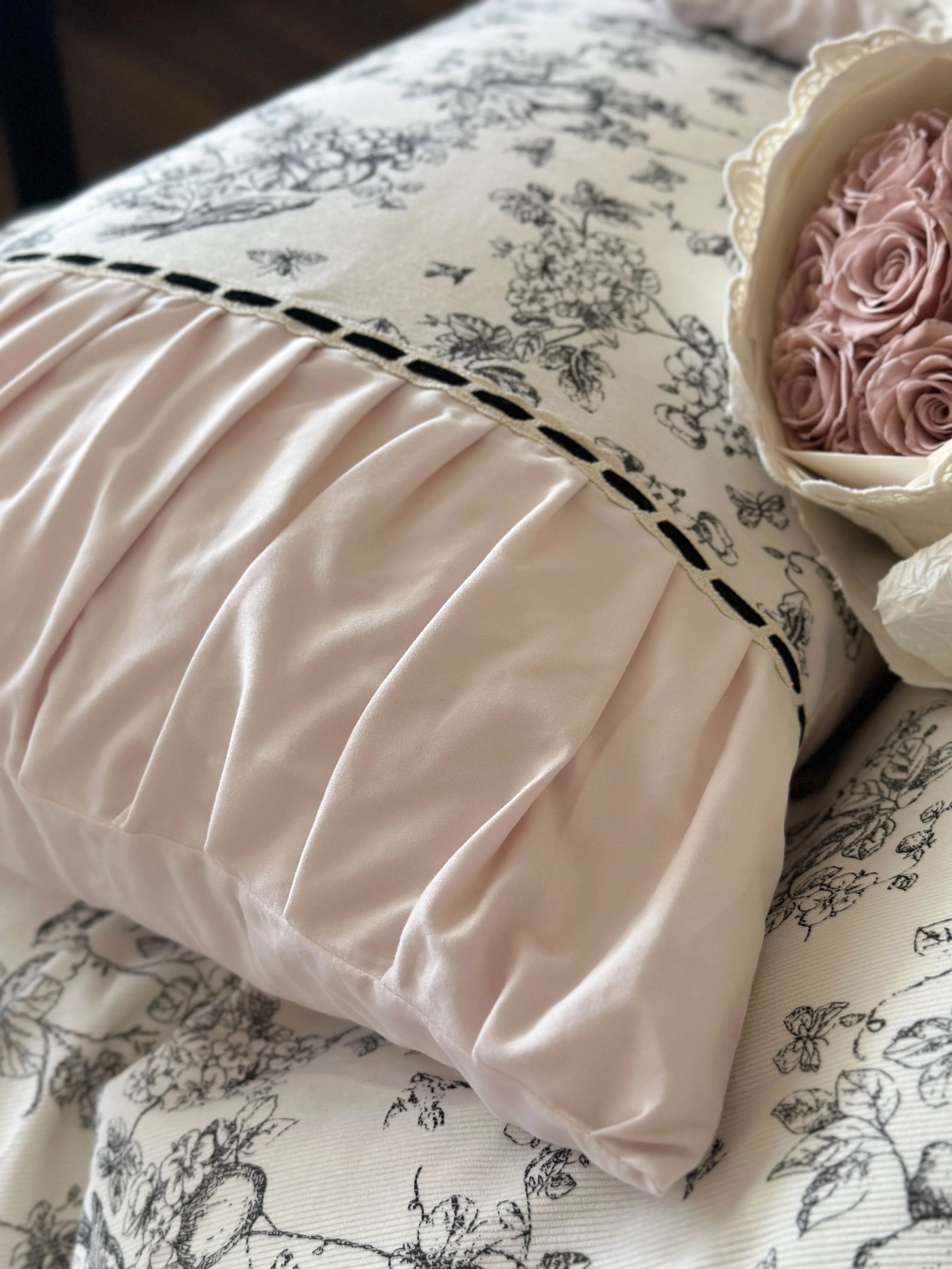 Macro shot of the soft pink ruched pillow from the Pink Toile bedding set with a rose bouquet nearby. - RoomDen