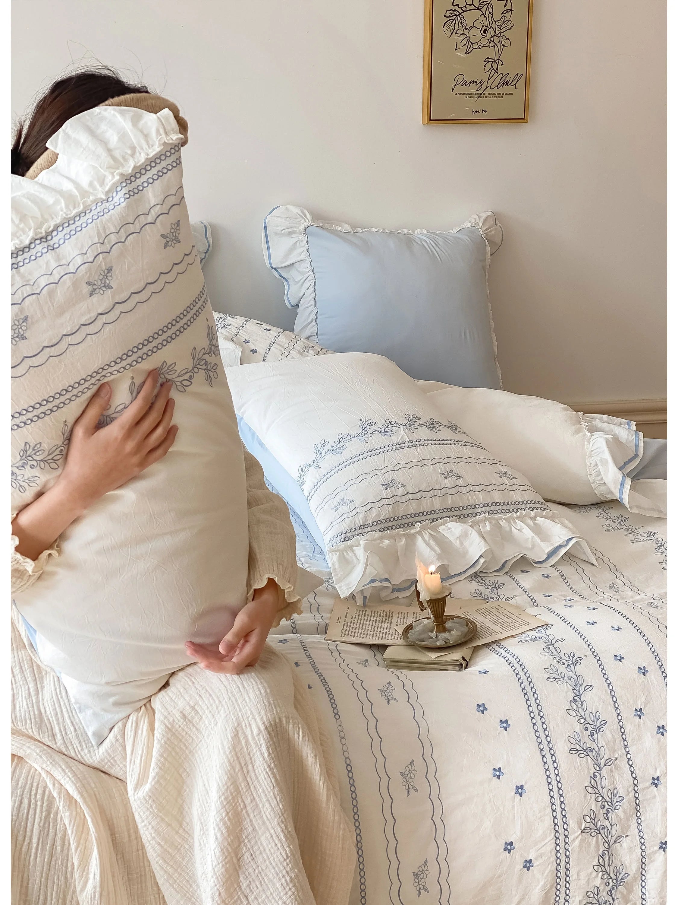 A person hugging a ruffled and embroidered pillow from the Cornflower Blue bedding set.