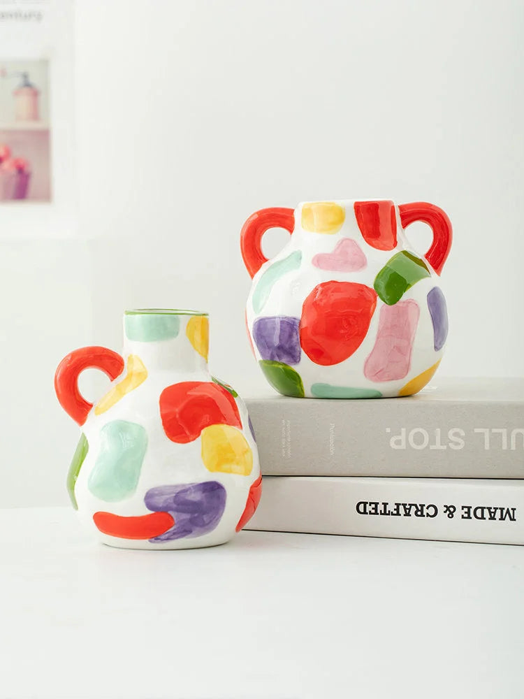 The double-handle and single-handle spotty ceramic vases styled together on a stack of books. - RoomDen