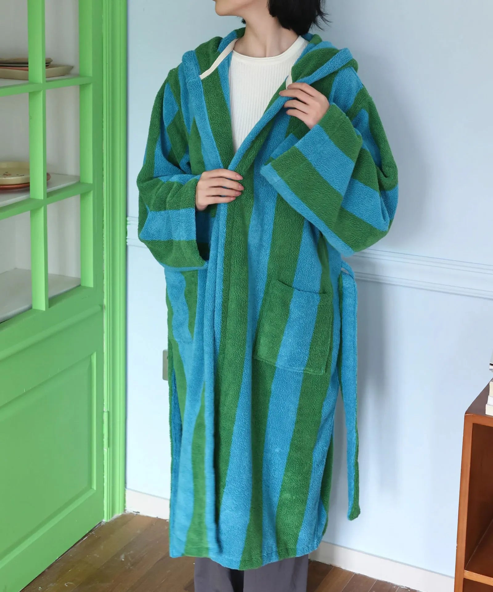 Woman tying the belt of a plush green and blue striped hooded robe - RoomDen