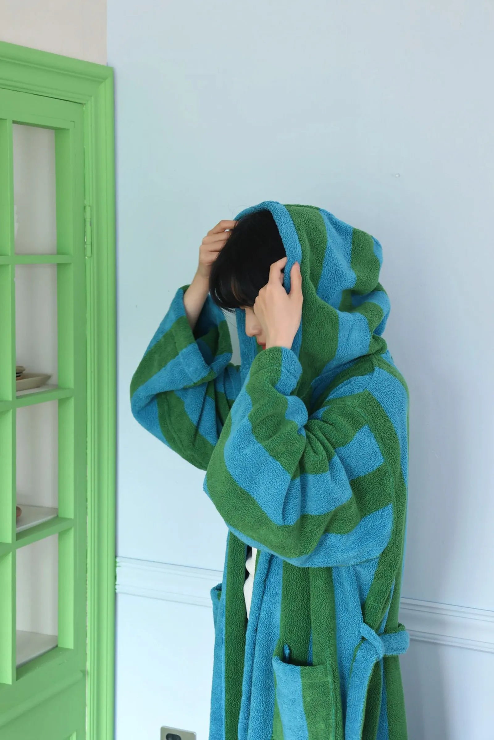 Side view of a woman wearing a blue and green striped terry cloth robe with hood up - RoomDen