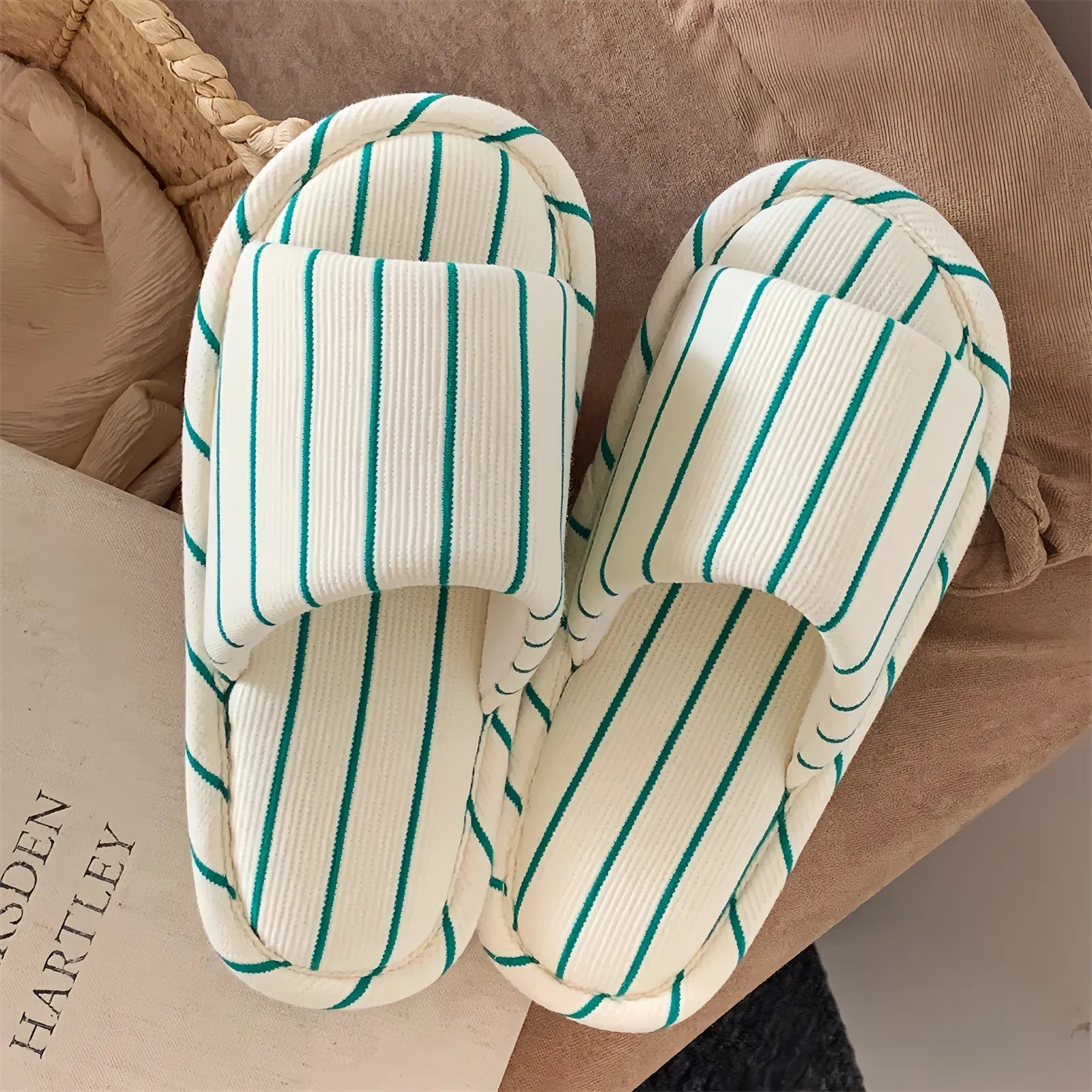 A pair of Green & White Striped Cotton House Slippers placed on a book, highlighting the clean minimalist design.