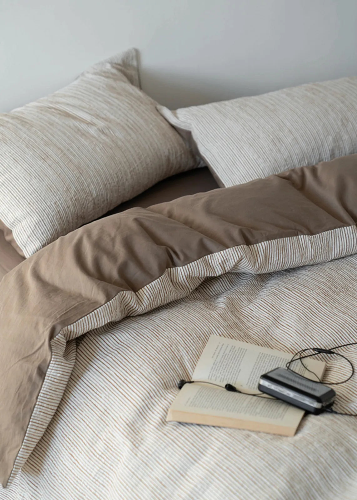 Close-up of the Latte Brown pinstripe bedding with an open book, showcasing its soft texture - RoomDen
