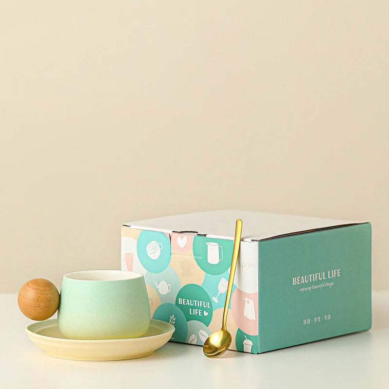 The Mint Green gradient ceramic mug and saucer set with a golden spoon, shown next to its stylish gift box. - RoomDen