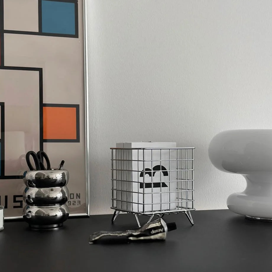 Minimalist grid metal desktop organizer on a black desk next to a modern chrome pen holder and framed art - RoomDen.