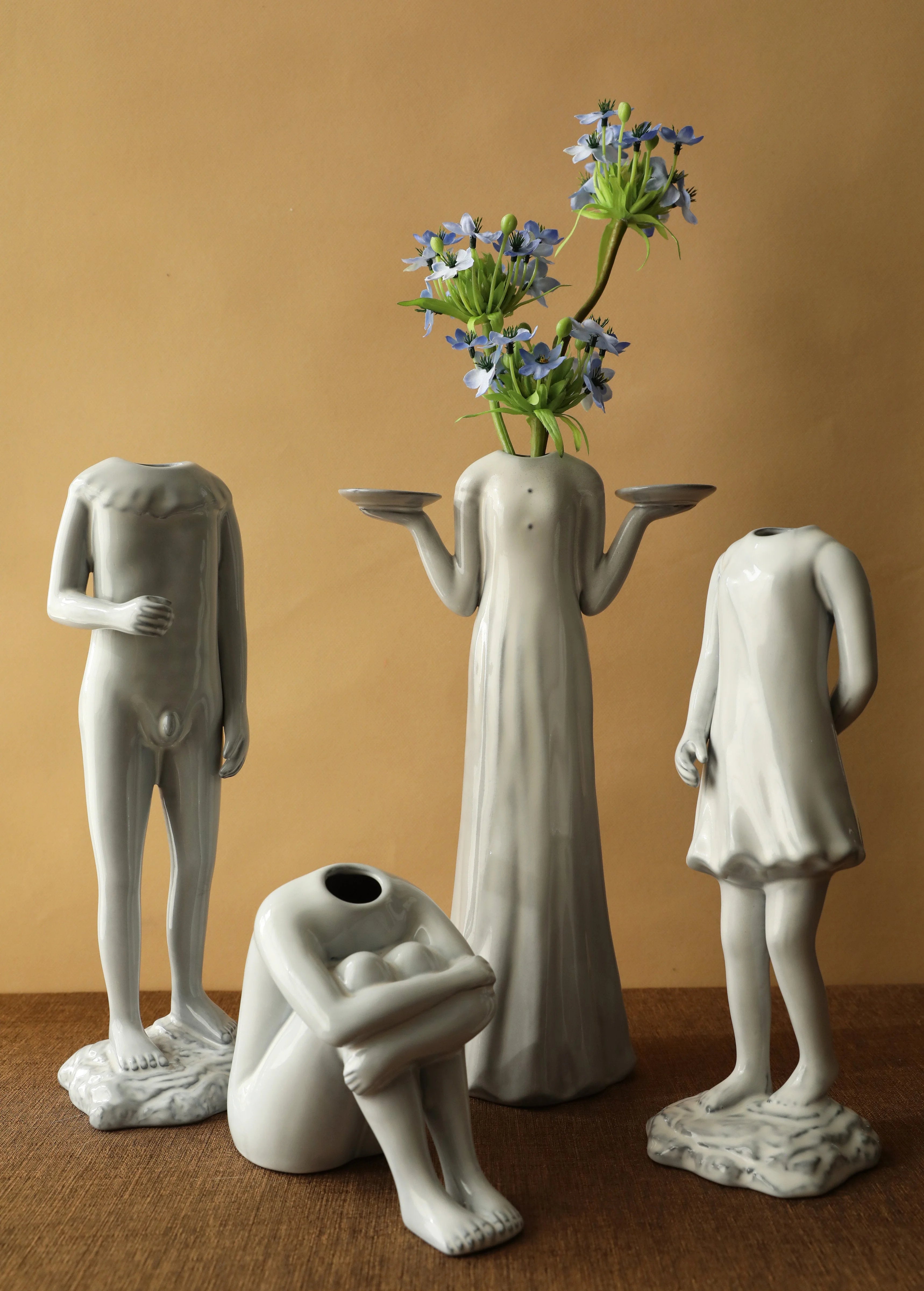 The full set of four human figure ceramic vases displayed together, one holding blue flowers. - RoomDen