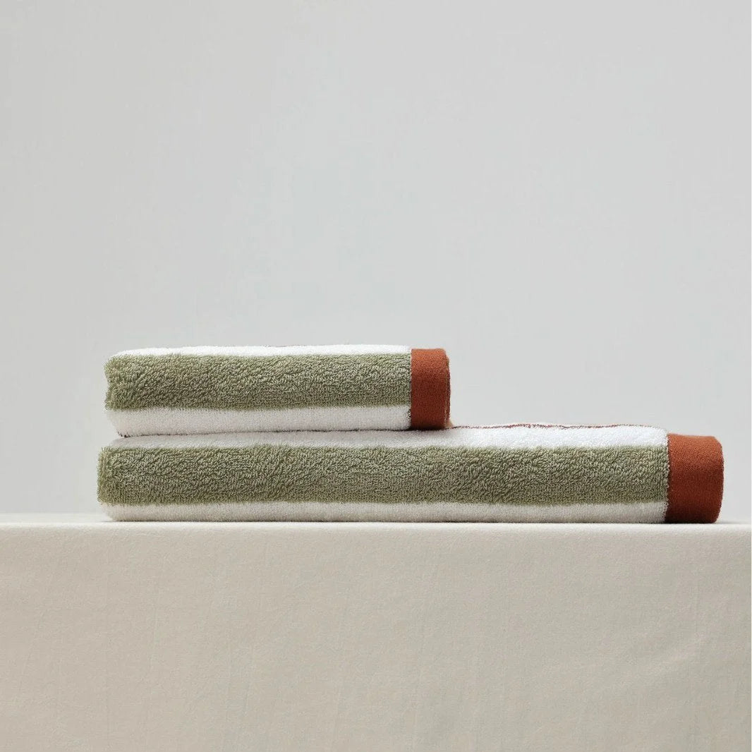 Folded green and white striped cotton face towel and bath towel stacked on a neutral surface - RoomDen